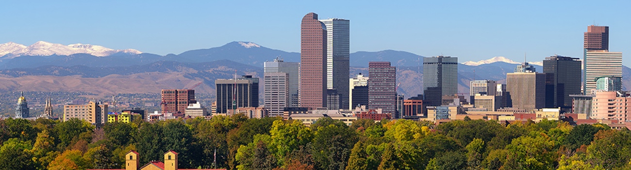Skyline of Denver, Colorado. Bright daytime sun. Rocky Mountains in the distance to the west.
